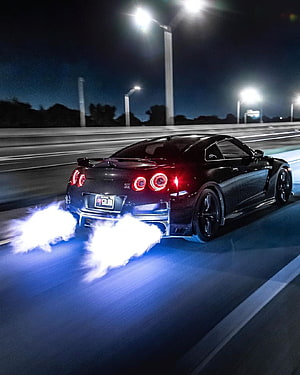 Nissan Skyline GT-R performing a burnout on a highway at night with glowing exhaust flames HD phone wallpaper