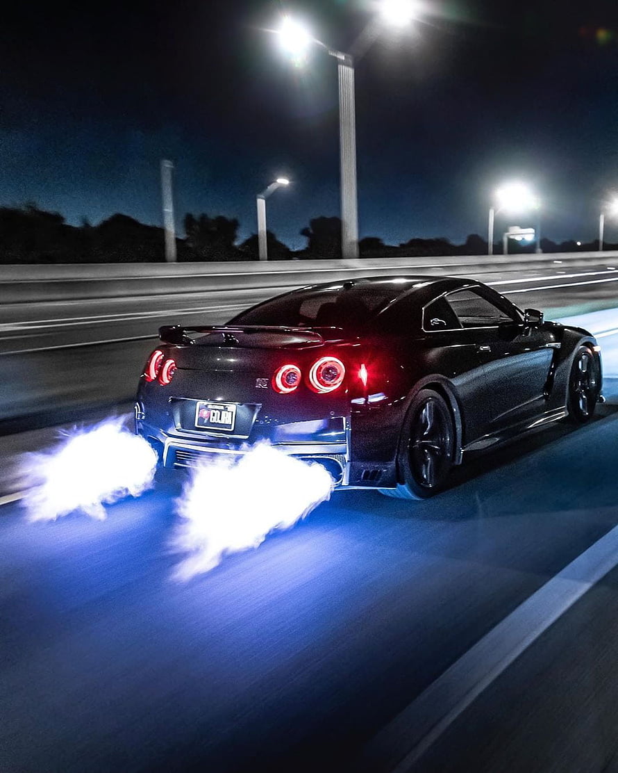 Nissan Skyline GT-R performing a burnout on a highway at night with glowing exhaust flames HD phone wallpaper