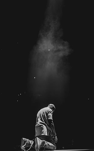 Kanye West kneeling on stage under dramatic smoke during the Yeezus Tour in black and white HD phone wallpaper