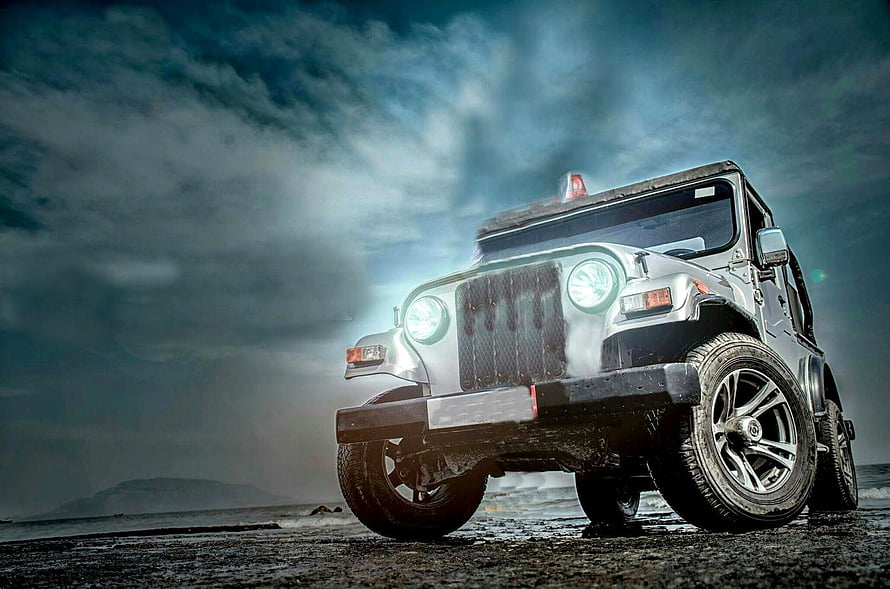 Silver Jeep Wrangler with glowing headlights on a wet beach under a dramatic stormy sky HD wallpaper