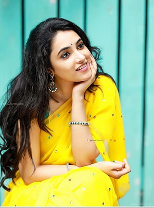 Priyanka Arul Mohan in a bright yellow saree with traditional jewelry against a teal background HD phone wallpaper