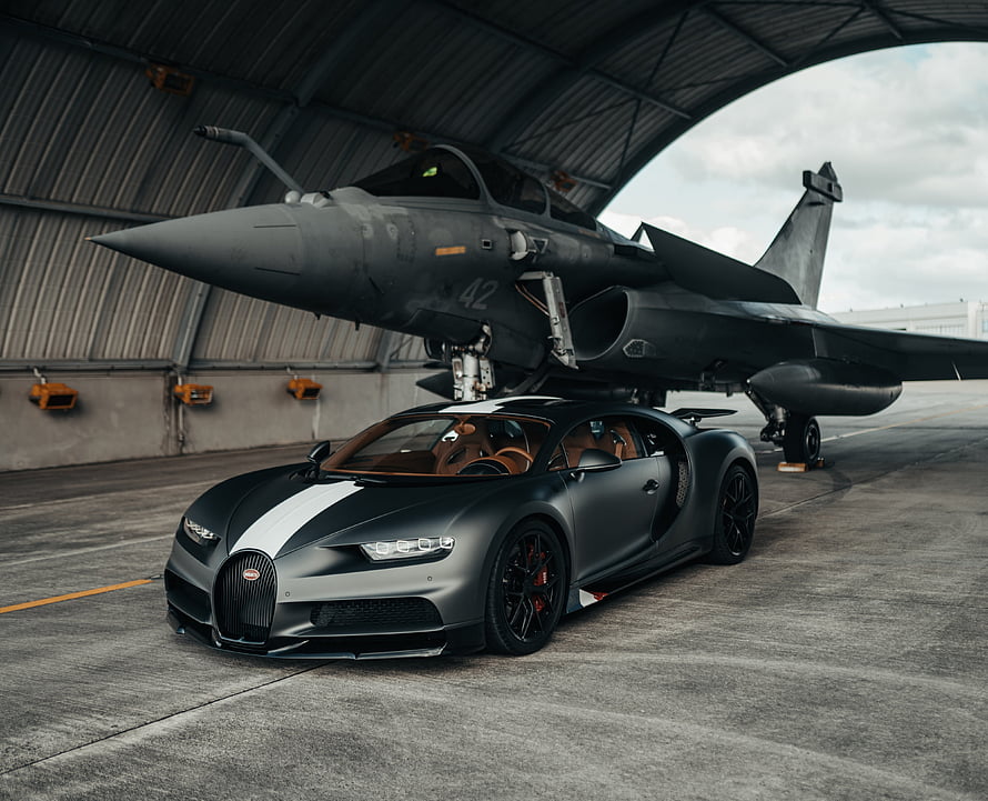 Matte Black Bugatti Chiron Parked in Front of a Stealth Fighter Jet Inside a Hangar HD wallpaper