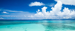Turquoise Lagoon and Deep Blue Ocean Under a Bright Sky with Fluffy Clouds HD wallpaper