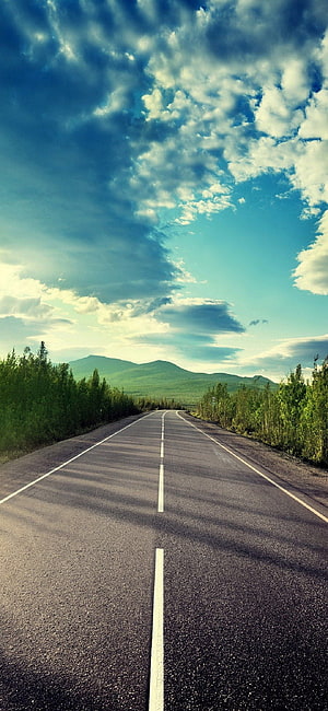 Empty Highway Stretching Toward Distant Green Hills Under a Dramatic Cloudy Sky HD phone wallpaper