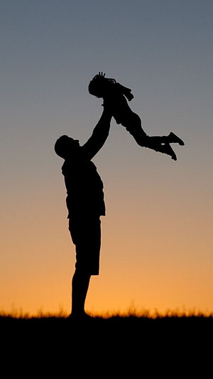 Silhouette of a father tossing a child into the air against a warm sunset sky HD phone wallpaper