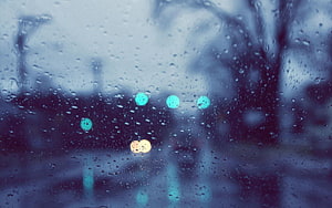 Raindrops on a glass window with blurred city lights and bokeh in a cool blue tone HD wallpaper
