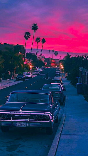 Retro Street Scene at Dusk with Classic Cars and Palm Trees Under a Vibrant Pink Sky HD phone wallpaper