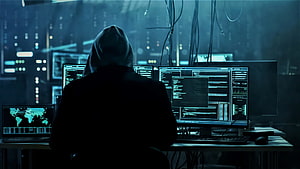 Silhouette of a hooded hacker at a multi-monitor workstation in a dark cyber room HD wallpaper