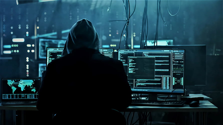 Silhouette of a hooded hacker at a multi-monitor workstation in a dark cyber room HD wallpaper