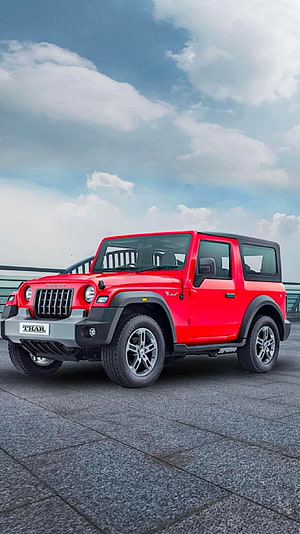 Red Mahindra Thar SUV parked on a paved plaza under a cloudy blue sky HD phone wallpaper