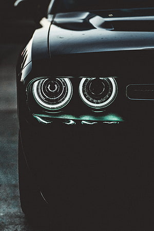 Close-up of a black car's dual circular LED headlights glowing in the dark HD phone wallpaper