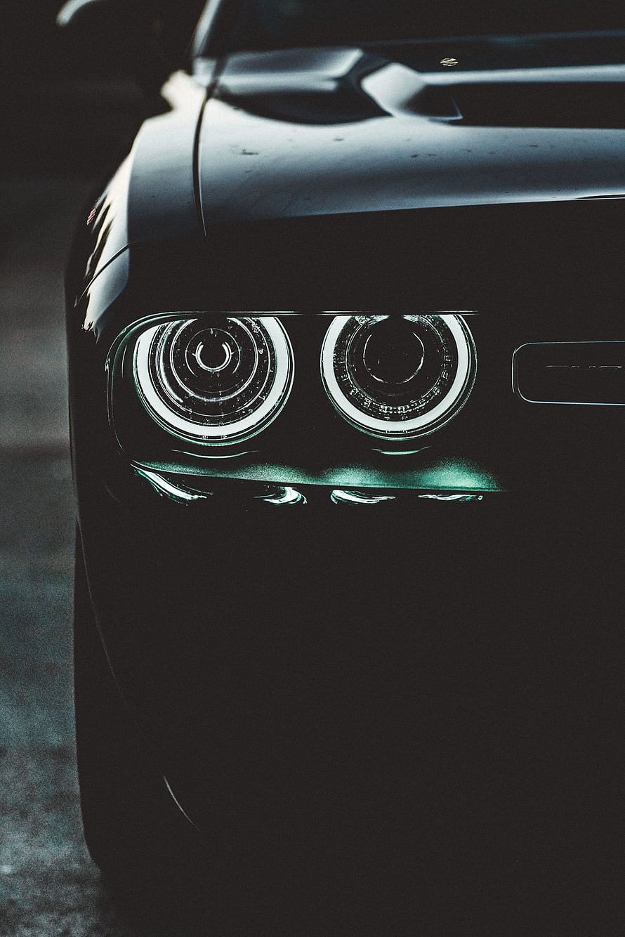 Close-up of a black car's dual circular LED headlights glowing in the dark HD phone wallpaper