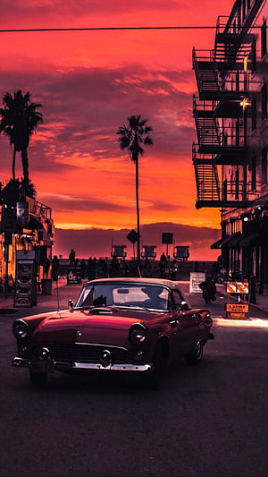 Vintage American Car on a Coastal Street at Sunset with Palm Trees and Beach Cabins HD phone wallpaper