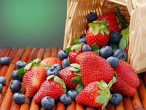 Fresh strawberries and blueberries spilling from a wicker basket on a wooden surface HD wallpaper
