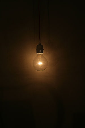 Glowing vintage filament bulb hanging from a dark textured wall in moody low light HD phone wallpaper