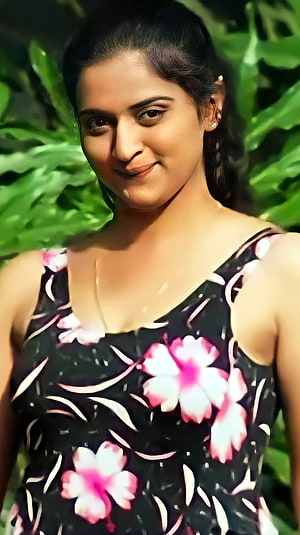 Pavitra Lokesh in a floral dress with a soft smile against a lush green leafy background HD phone wallpaper