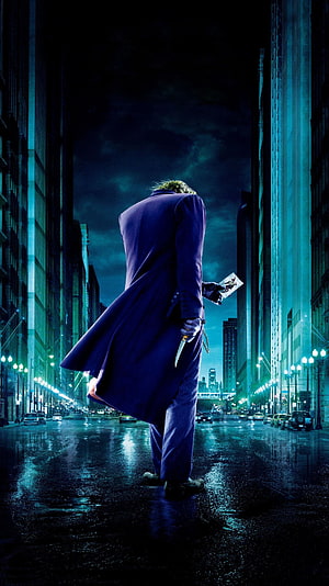 Joker from The Dark Knight standing in a rain-soaked city street at night holding a knife and playing card HD phone wallpaper