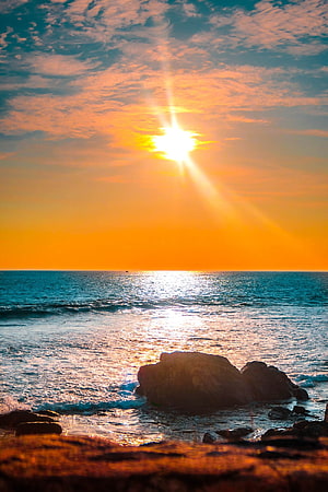 Golden sunrise over the ocean with sun rays illuminating coastal rocks and waves HD phone wallpaper