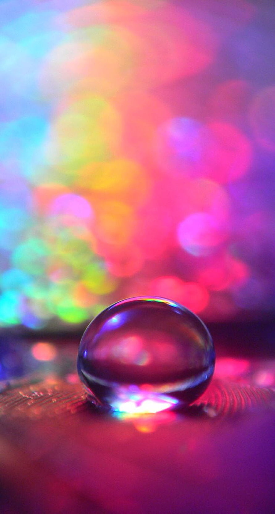 Vibrant Bokeh Lights Behind a Clear Glass Sphere on a Textured Surface HD phone wallpaper