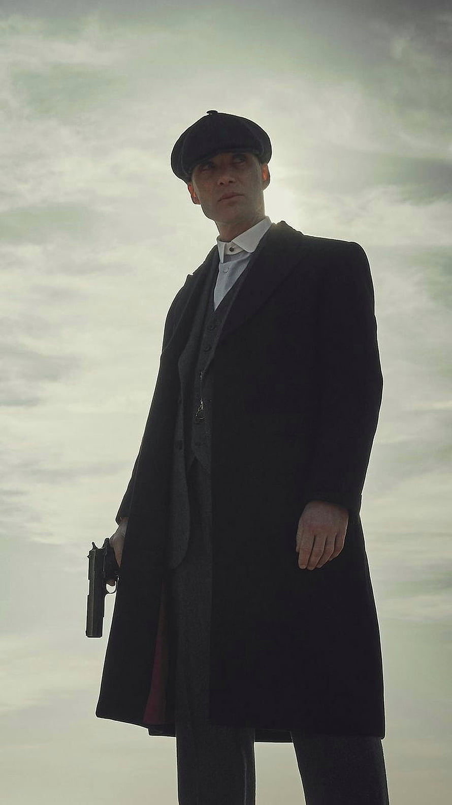 Tommy Shelby from Peaky Blinders in a long coat and flat cap holding a pistol against a cloudy sky HD phone wallpaper