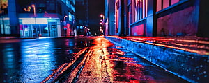 Neon-lit wet city street at night with vivid blue and red reflections on rain-slicked asphalt HD wallpaper