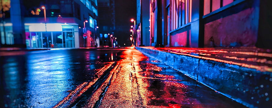 Neon-lit wet city street at night with vivid blue and red reflections on rain-slicked asphalt HD wallpaper