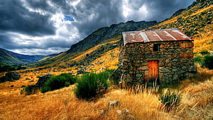 Rustic Stone Cabin with Corrugated Roof in Golden Mountain Valley Under Dramatic Storm Clouds HD wallpaper