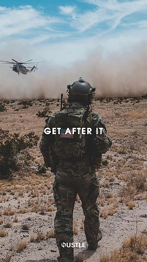 Soldier in Camouflage Gear Walking Through Desert with Helicopter in Background HD phone wallpaper
