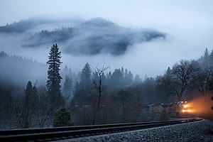 Freight train navigating foggy mountain railway at dawn with glowing headlights HD wallpaper