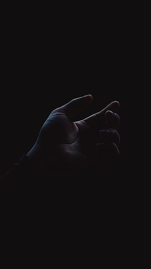 Dramatic Silhouette of a Reaching Hand Against a Deep Black Background HD phone wallpaper