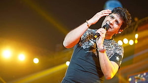 Krishnakumar Kunnath performing live on stage with microphone and warm concert lighting HD wallpaper