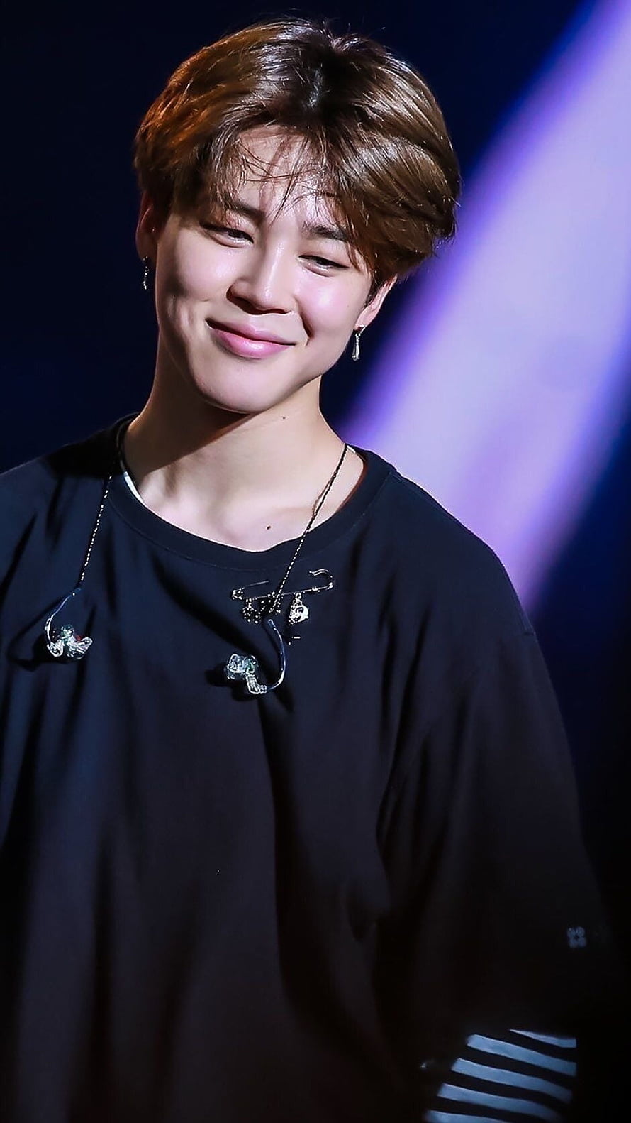 Jimin from BTS smiling on stage in a black t-shirt with in-ear monitors and silver jewelry HD phone wallpaper