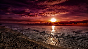 Dramatic Crimson Sunset Over a Quiet Sandy Shoreline with Cloudy Sky HD wallpaper