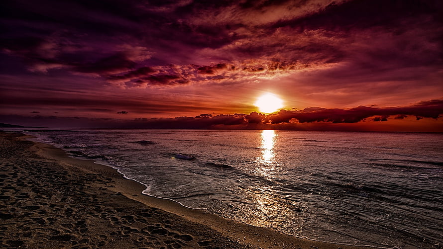 Dramatic Crimson Sunset Over a Quiet Sandy Shoreline with Cloudy Sky HD wallpaper