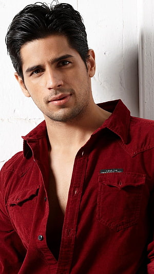Siddharth Malhotra in a deep red corduroy shirt against a white brick wall HD phone wallpaper