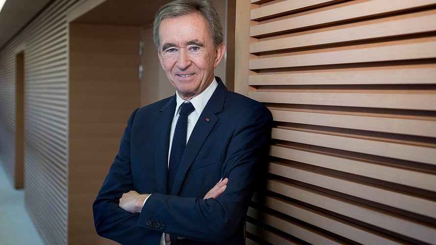 Bernard Arnault in a dark suit leaning against a wooden slat wall with arms crossed HD wallpaper