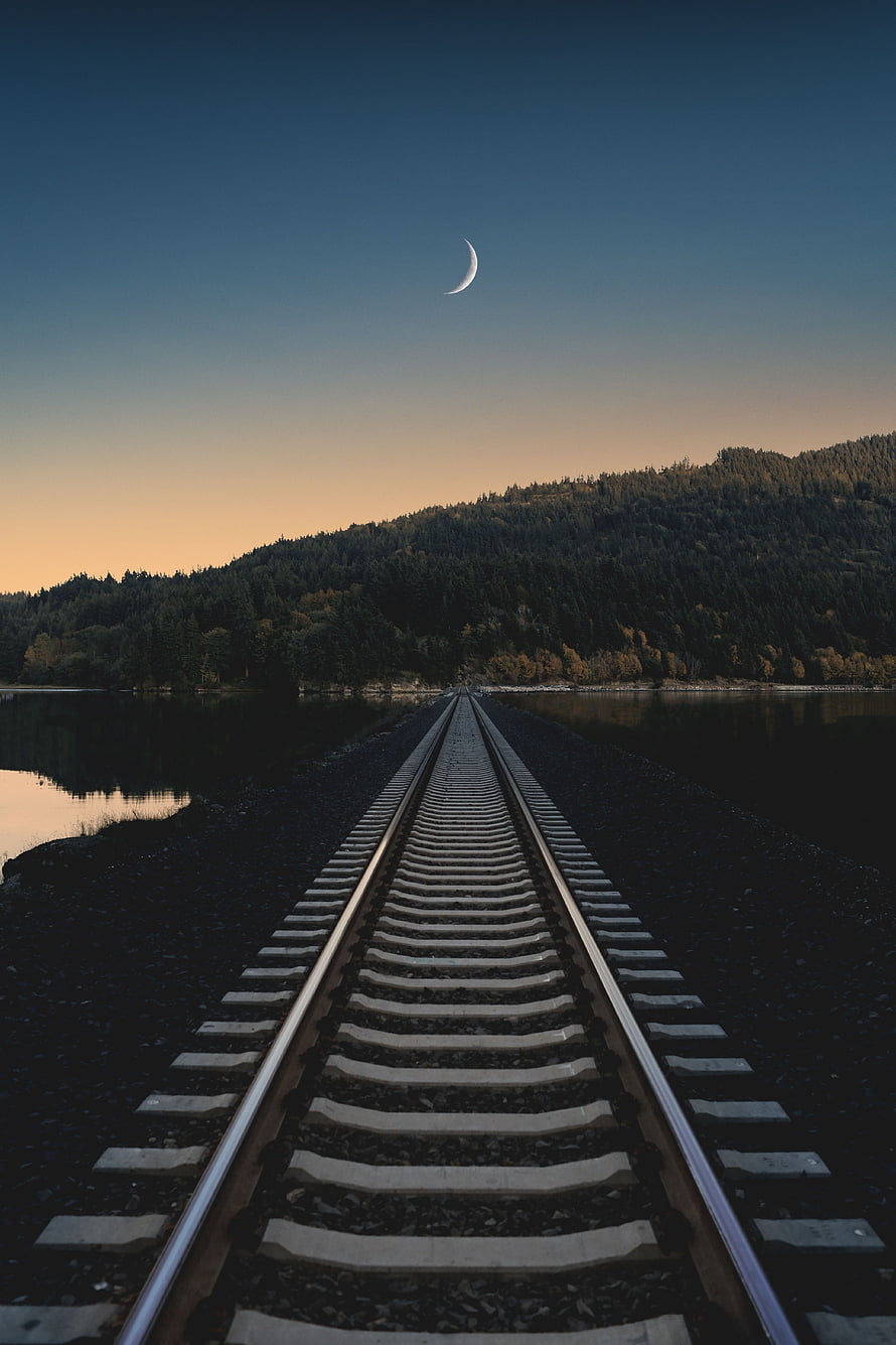 Railway Tracks Leading to a Forested Hill at Dusk with a Crescent Moon HD phone wallpaper