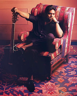Yuvan Shankar Raja seated in a patterned armchair holding an acoustic guitar HD phone wallpaper