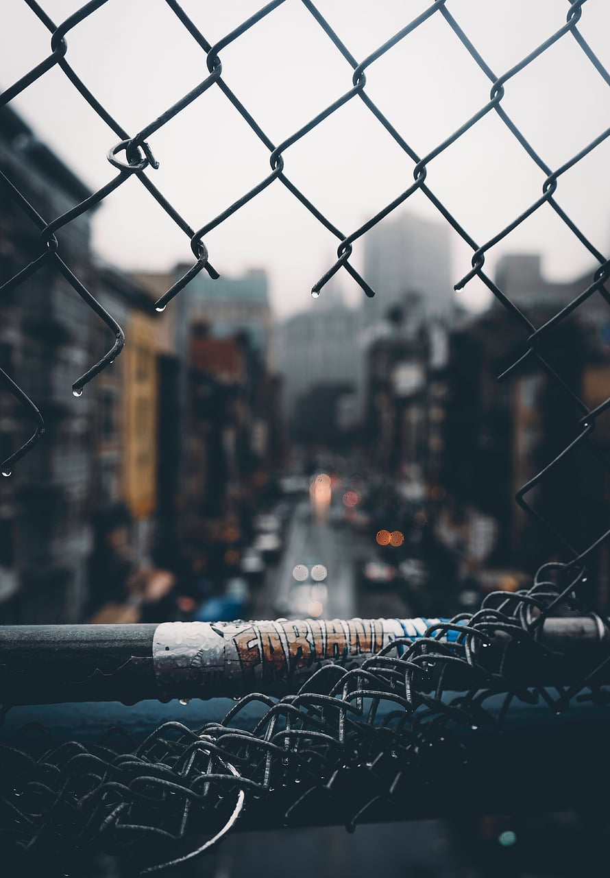 Moody Urban Street View Through Rainy Chain Link Fence With Bokeh Lights HD phone wallpaper