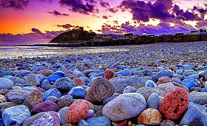 Vibrant pebble beach at sunset with dramatic purple and orange sky over coastal town HD wallpaper