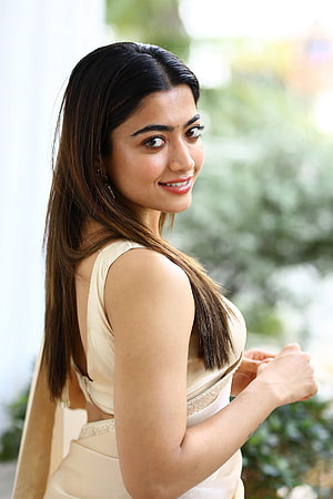 Rashmika Mandanna in a cream saree with a soft smile and natural outdoor backdrop HD phone wallpaper