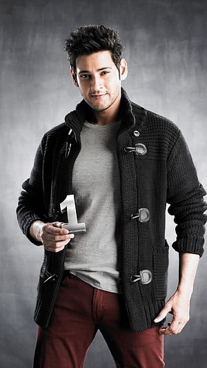 Mahesh Babu in a black duffle coat holding a silver number one prop against a grey studio backdrop HD phone wallpaper