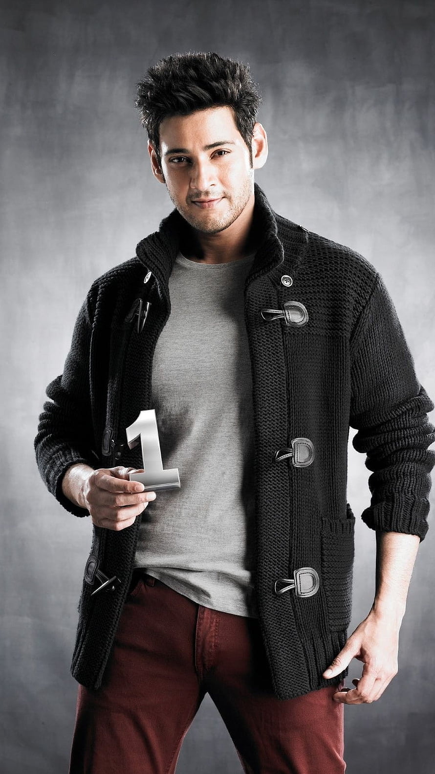 Mahesh Babu in a black duffle coat holding a silver number one prop against a grey studio backdrop HD phone wallpaper