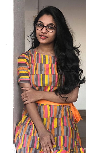Aleena Shaji in a colorful striped dress with long dark hair and glasses HD phone wallpaper