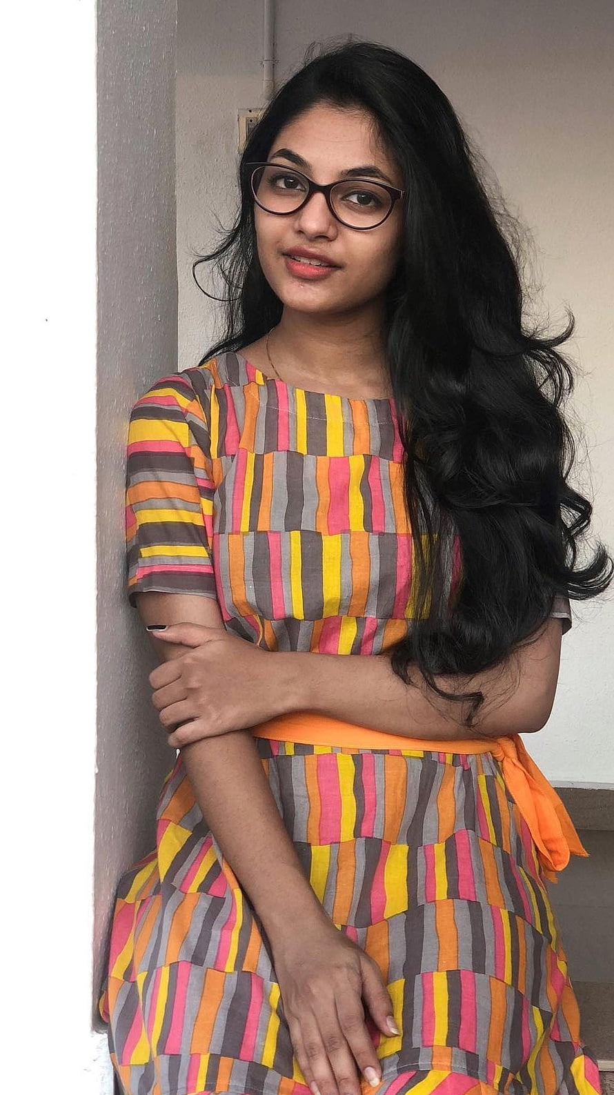 Aleena Shaji in a colorful striped dress with long dark hair and glasses HD phone wallpaper