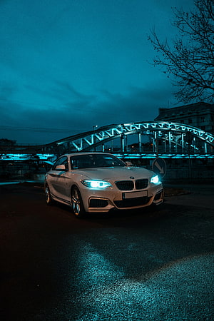 White BMW 2 Series Coupe with Glowing Headlights Parked Under an Illuminated Bridge at Night HD phone wallpaper