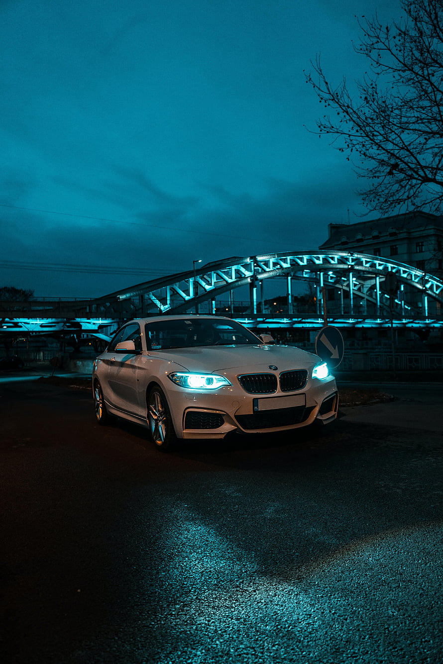 White BMW 2 Series Coupe with Glowing Headlights Parked Under an Illuminated Bridge at Night HD phone wallpaper