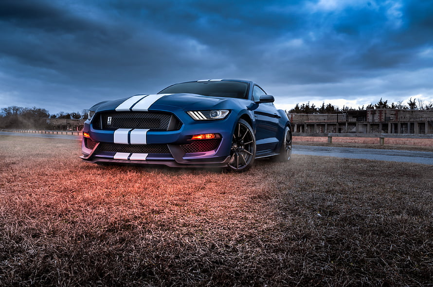 Blue Ford Mustang Shelby GT500 with white racing stripes parked on dry grass under a dramatic stormy sky HD wallpaper