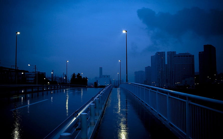 Moody Nighttime Cityscape on a Wet Bridge with Glowing Streetlights and Rain-Soaked Reflections HD wallpaper
