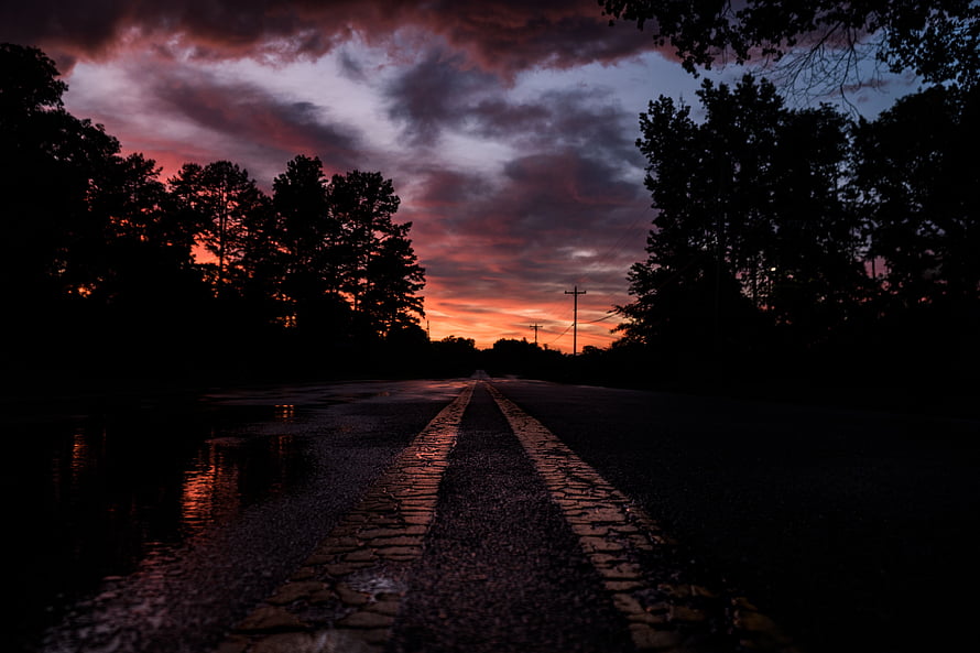 Moody Country Road at Dusk with Dramatic Sunset Sky and Silhouetted Trees HD wallpaper